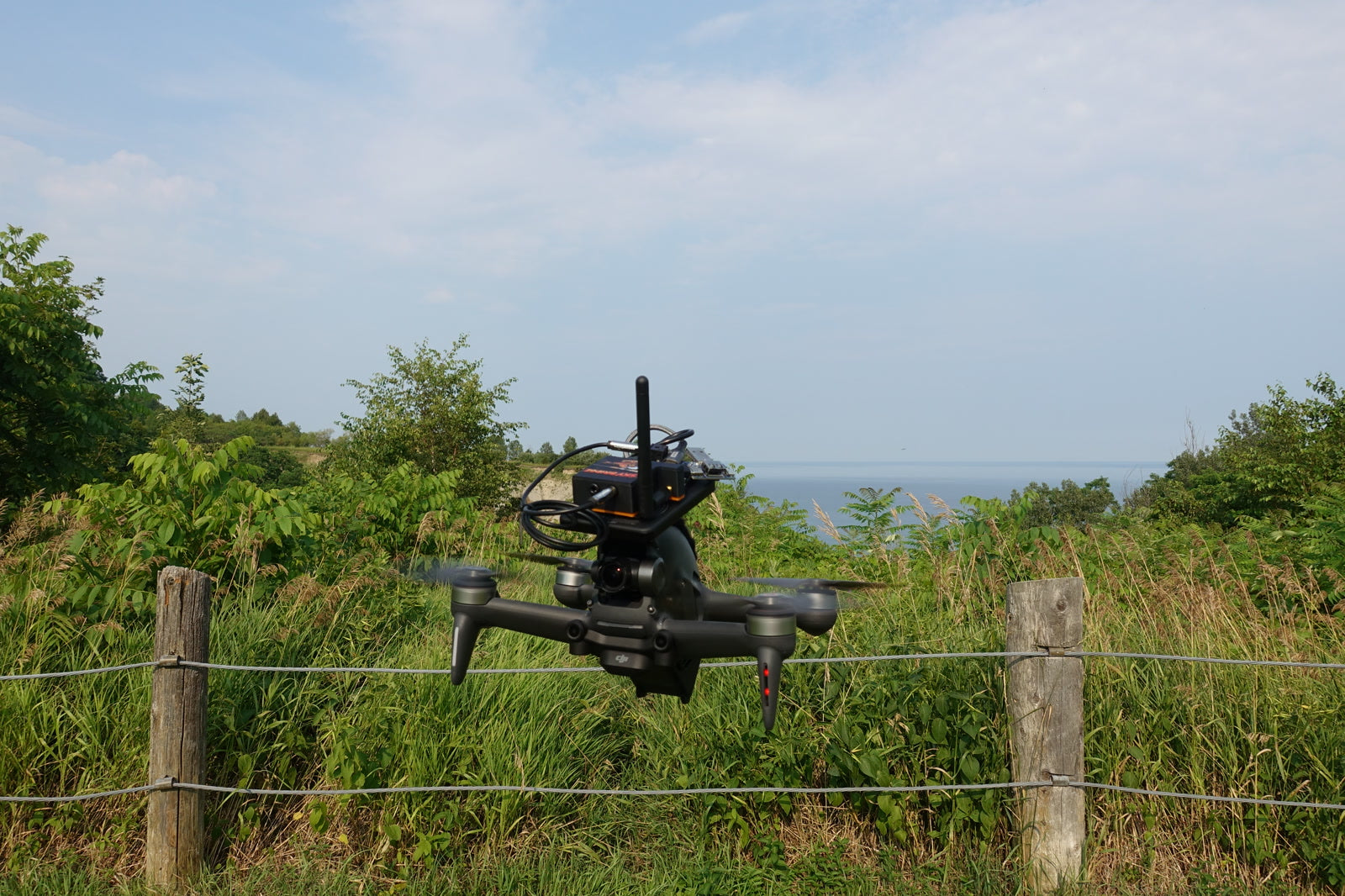 Sky Bridge riding a drone over a meadow, Lake Ontario behind